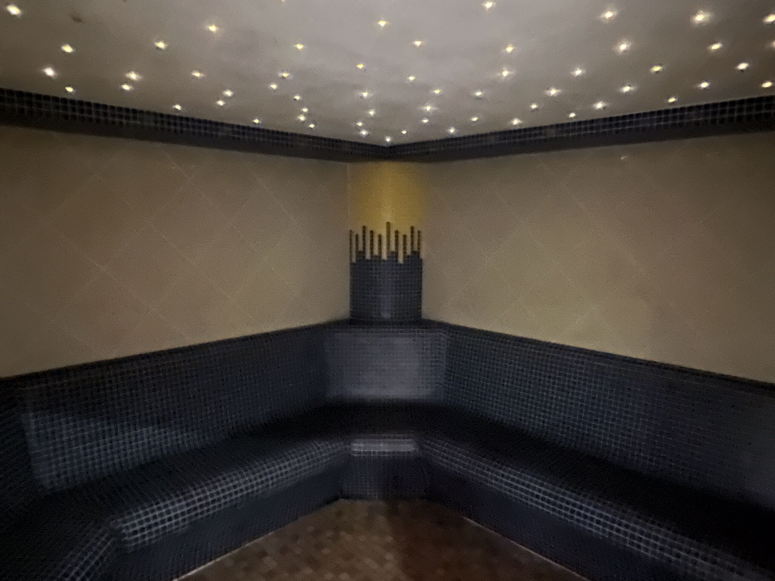Ein Zimmer mit einer dunkelblauen gefliesten Bank, einer strukturierten Wand und einer Decke mit Einbuchtungslampen.