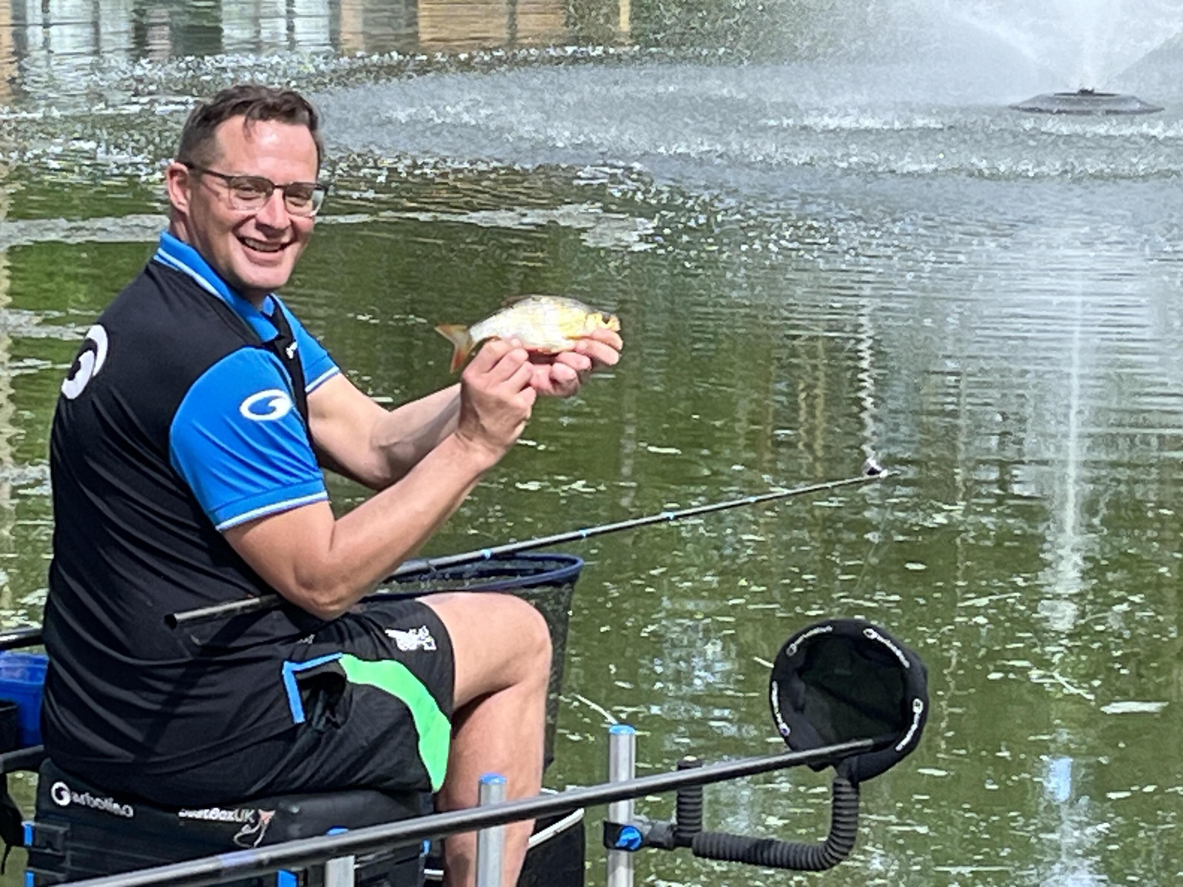 A person sitting on a chair by a body of water, holding a fish.