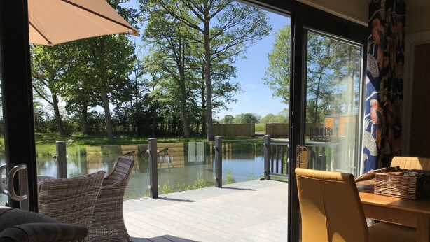 A deck with wicker chairs and a table, overlooking a lake and trees. - Pine Boutique Lodge With hot tub for Couples & dog (York)