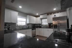 A modern kitchen with white cabinetry, a stainless steel refrigerator, and a granite countertop.