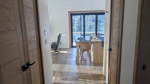 Ein Flur, der zu einem Zimmer mit Schreibtisch, Stuhl und großen Fenstern führt.