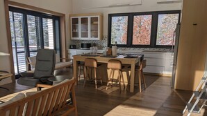 Eine moderne Küche mit Holzschränken, ein Essbereich mit Tisch und Stühlen sowie große Fenster mit Blick auf Bäume.