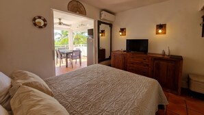 A bedroom with a bed, a TV, a wooden dresser, and a balcony with a table and chairs.