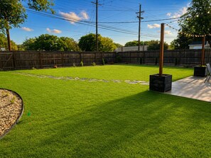 A backyard with a well-maintained lawn, stone pathway, wooden fence, and a patio area. - Coral Cottage by Park in Med Dst (Lubbock)