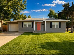 A single-story house with a red front door, a garage, and a well-maintained lawn. - Coral Cottage by Park in Med Dst (Lubbock)