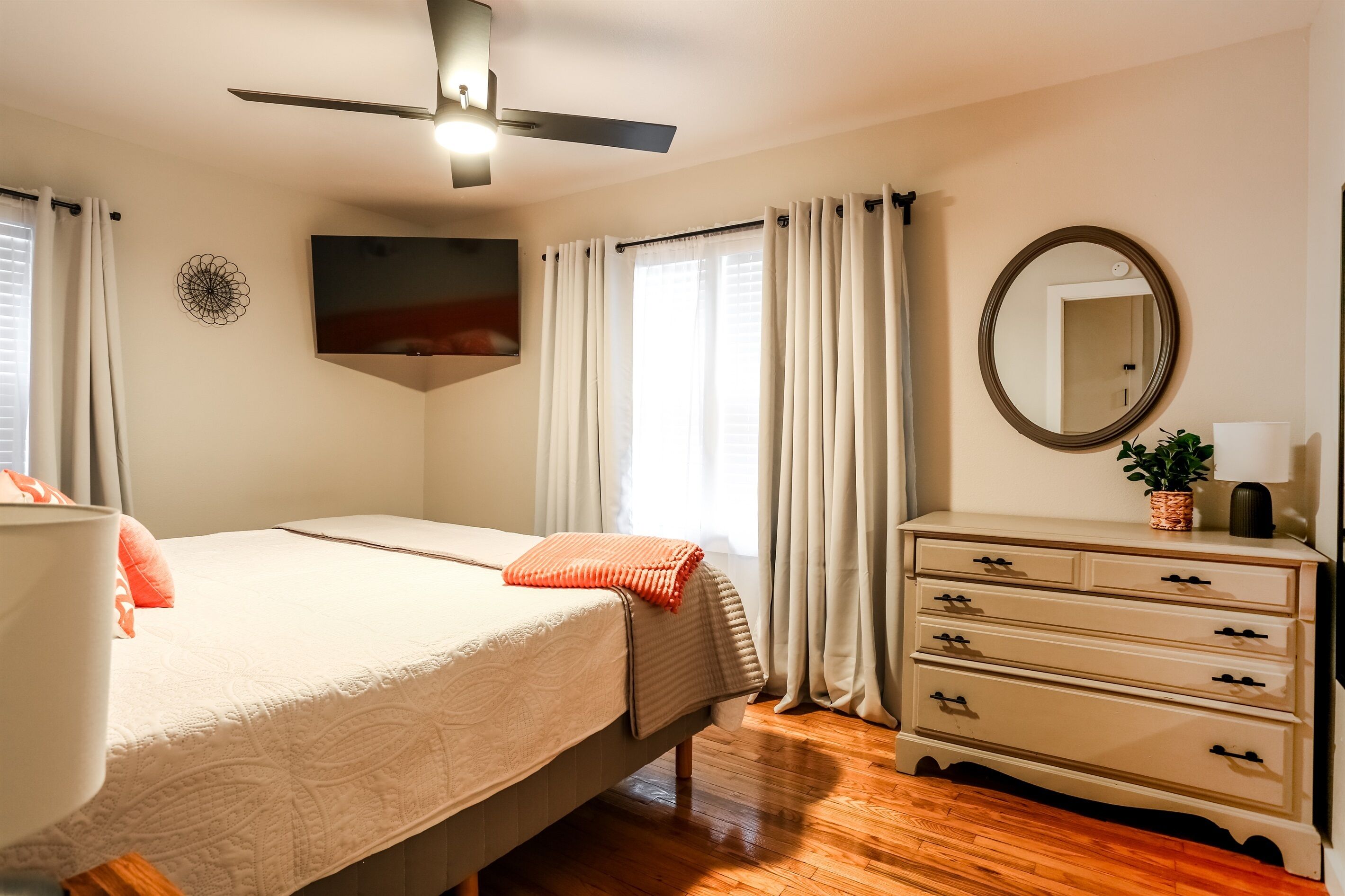 A bedroom with a bed, a dresser, a mirror, and a ceiling fan.