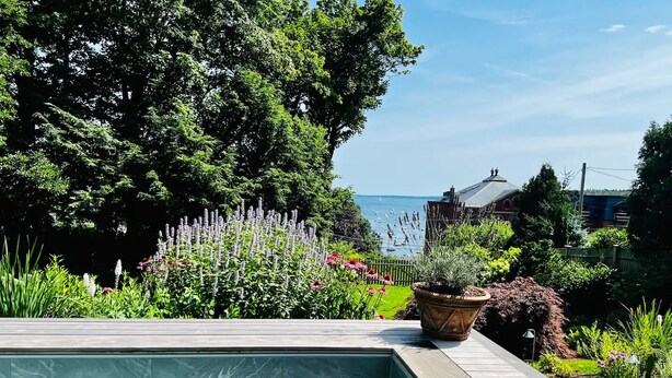 En swimmingpool med ett trädäck, omgiven av frodig grönska och med utsikt över havet.