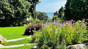 En välskött trädgård med ett stort utbud av blommor och växter, en stenlagd gång och en utsikt över havet i bakgrunden.