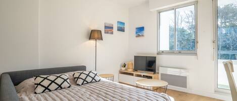 Quarto moderno com uma cama grande, uma televisão e uma janela com vista para árvores.