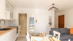 Een moderne keuken met een marmeren spatwand, een eethoek met een houten tafel en witte stoelen, en een grijze bank met oranje kussens.