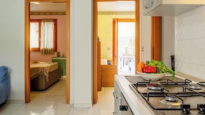 A modern kitchen with a gas stove, a dining area with a table and chairs, and a bedroom with a bed and a window. - Coraline Beach House (Mascali)
