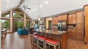 Une cuisine spacieuse avec des meubles de rangement en bois, un grand îlot central doté de tabourets, et un ventilateur de plafond.