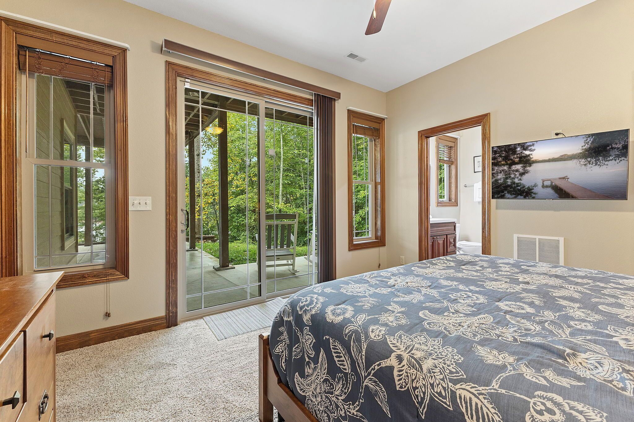 A bedroom with a large bed, a sliding glass door leading to a patio, and a painting on the wall.