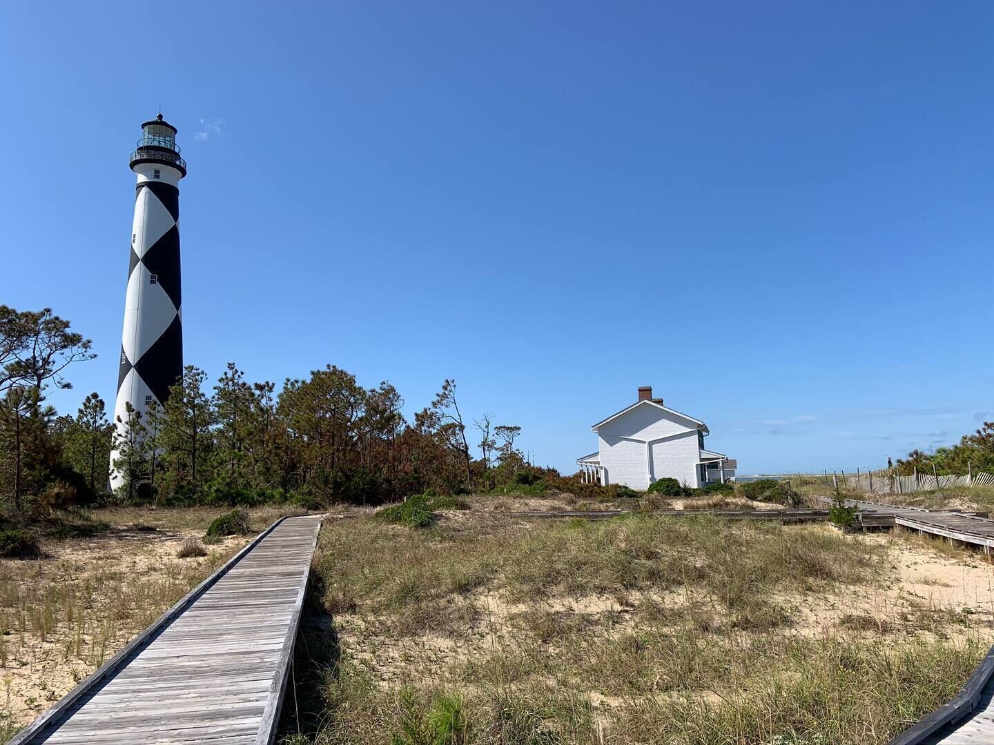 Un phare, un bâtiment blanc et une promenade en bois.