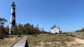 Un phare, un bâtiment blanc et une promenade en bois.