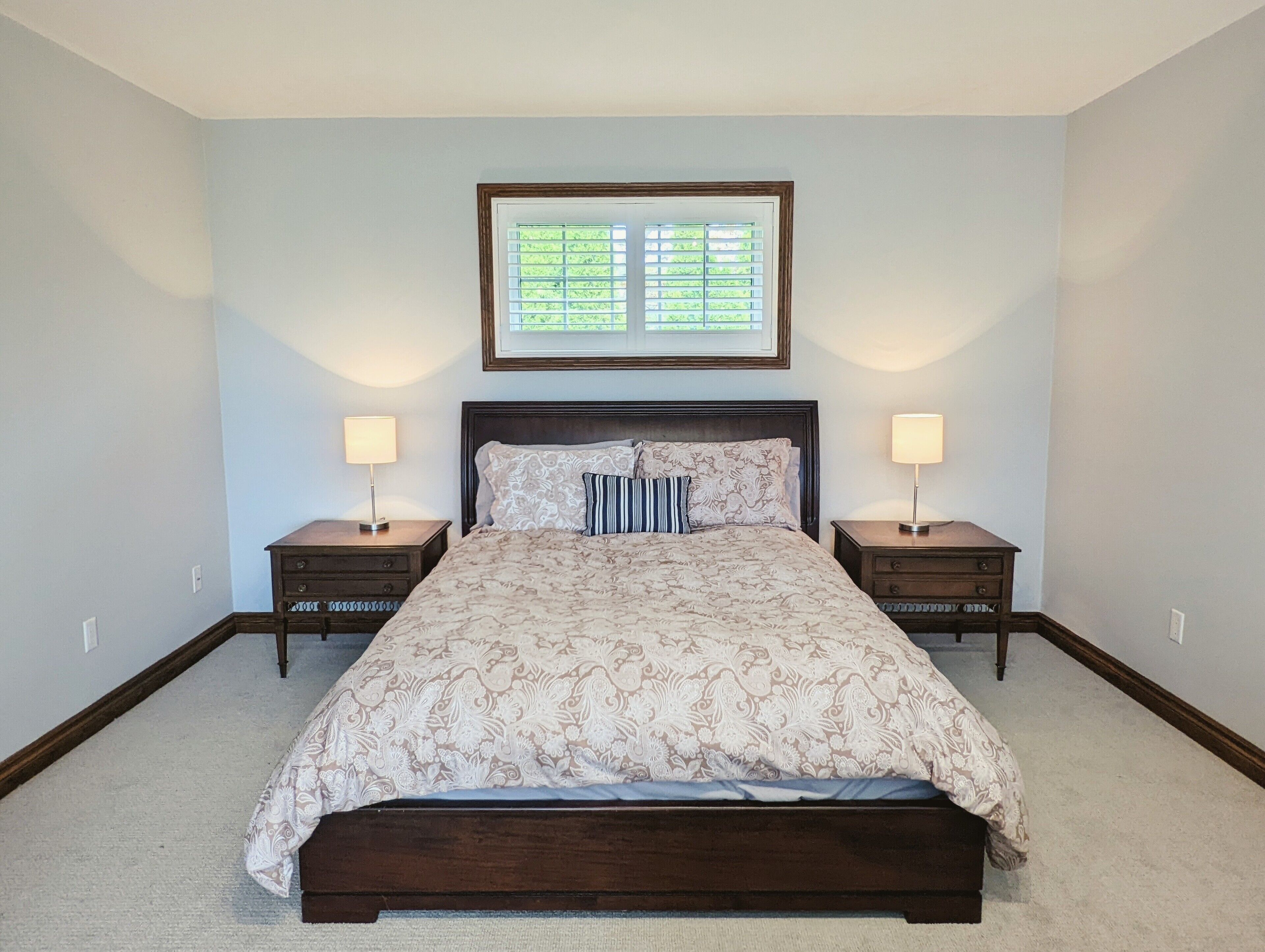 A bedroom with a large bed, two nightstands, and a window with blinds.