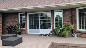 A brick building with a tiled roof, large windows, and a wooden deck with outdoor furniture and potted plants. - A poolside guest stay nested in a beautiful orchard along winery route (Niagara-on-the-Lake)