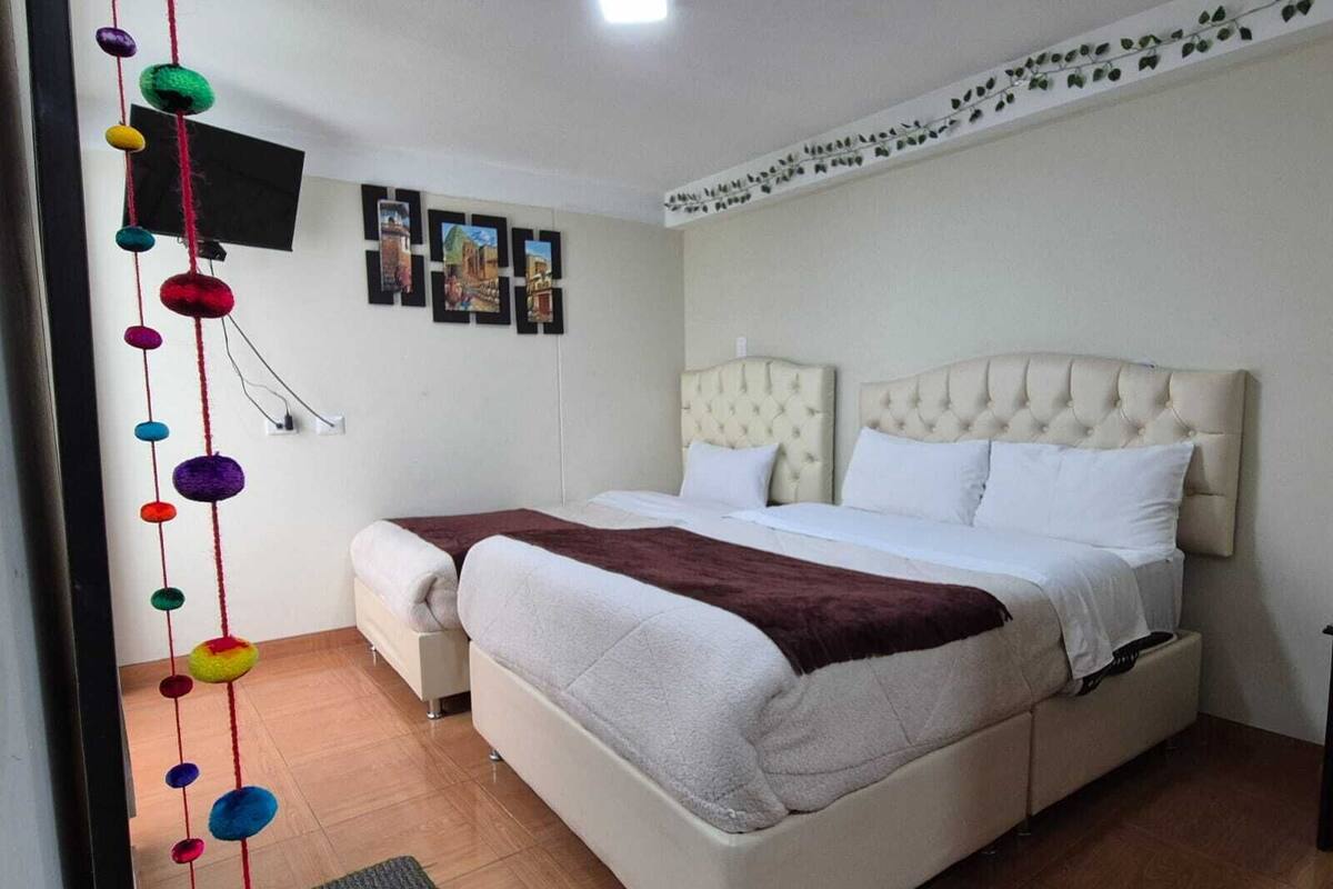 Een slaapkamer met een groot bed, een kleiner bed, een televisie aan de muur en een decoratieve slinger met kleurrijke ballen.
