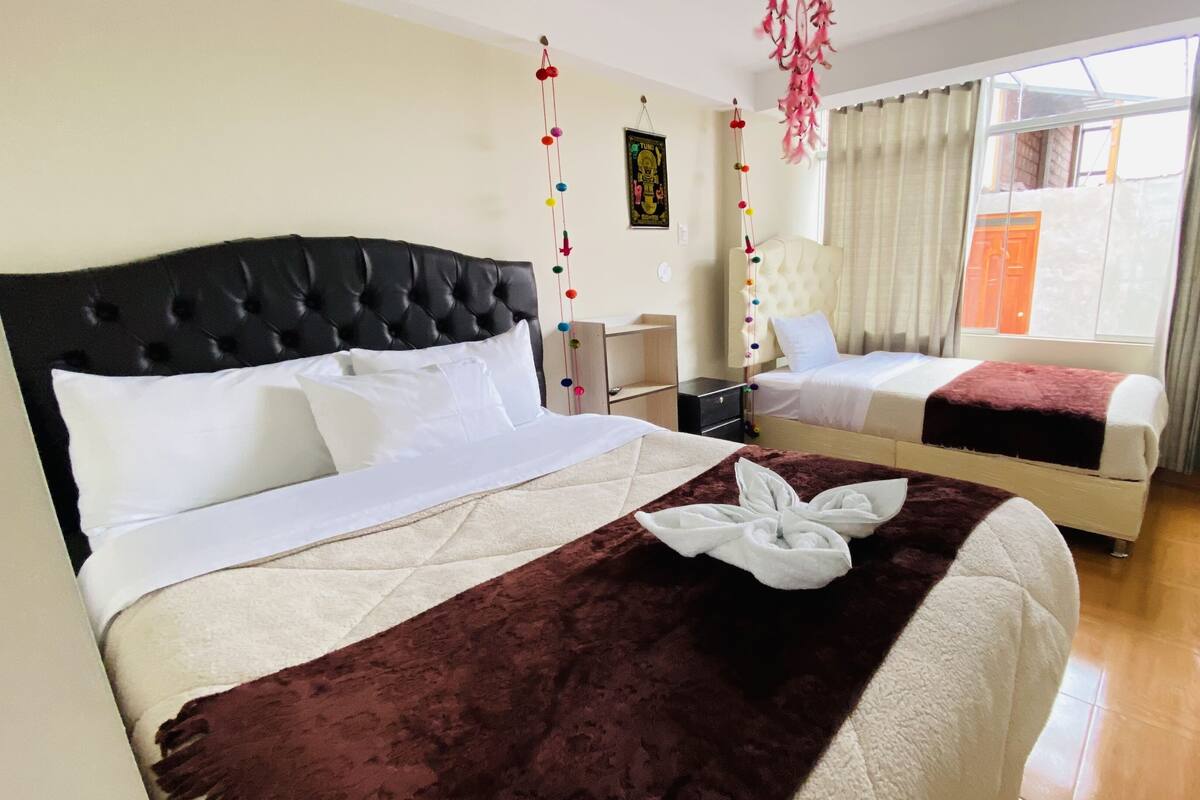Een hotelkamer met twee bedden, een zwart hoofdbord, een witte spreidek en een rode deken, plus een decoratieve handdoek op het bed.