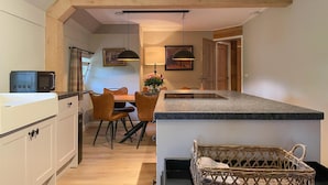 A modern kitchen with white cabinets, a dining area with a table and chairs, and a wicker chair. - Gorgeous home in Hellendoorn with sauna (Hellendoorn)