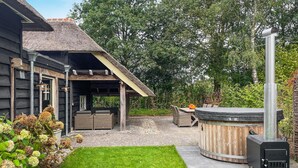 A wooden cabin with a thatched roof, outdoor seating area, and a wood-burning stove. - Gorgeous home in Hellendoorn with sauna (Hellendoorn)