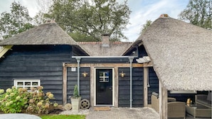 A rustic wooden building with thatched roofs, a black door, and a small porch area with outdoor seating. - Gorgeous home in Hellendoorn with sauna (Hellendoorn)