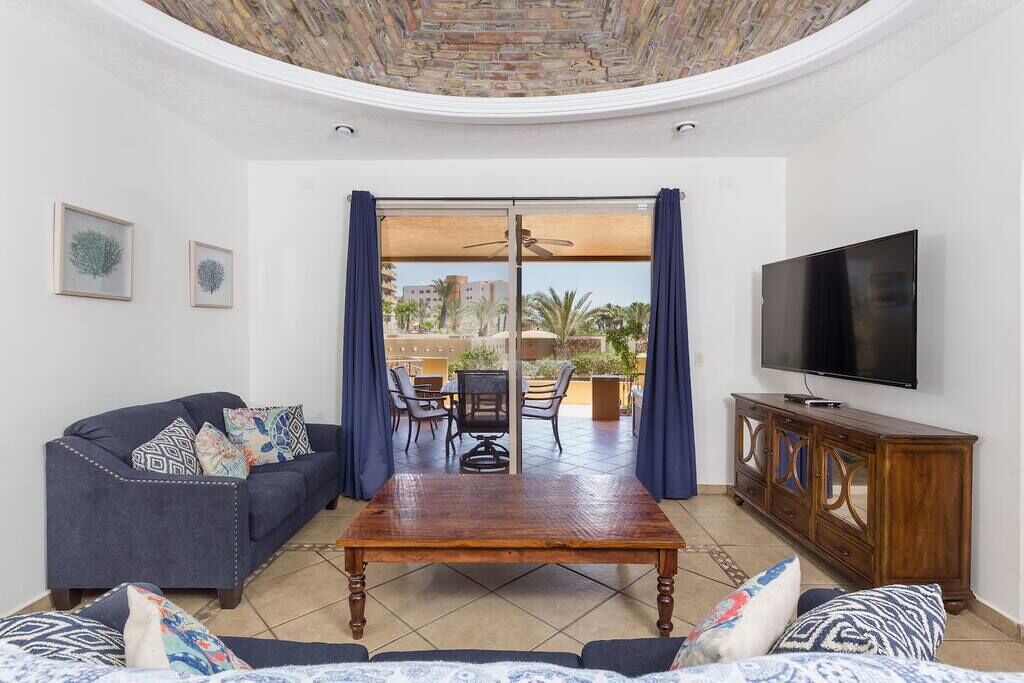 A living room with a sofa, a coffee table, a TV, and a view of the outdoors through a glass door.