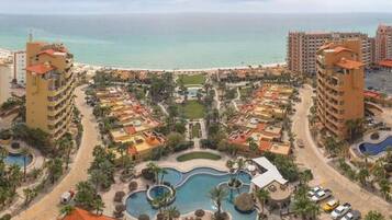 A resort with multiple buildings, a central pool area, and a beach view.