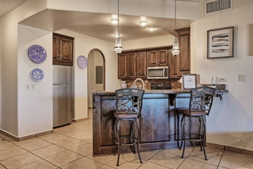 A kitchen with a central island, bar stools, wooden cabinets, a microwave, and a refrigerator.