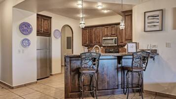 A kitchen with a central island, bar stools, wooden cabinets, a microwave, and a refrigerator.