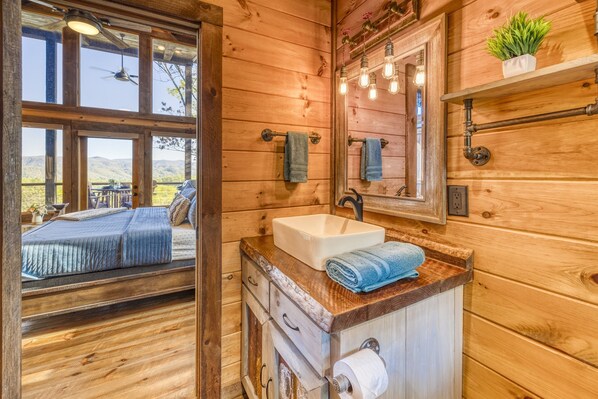 A wooden cabin bathroom with a large window, a sink, and a mirror.