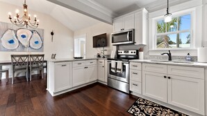 A modern kitchen with white cabinetry, stainless steel appliances, and a large window. - Main Street Pool and Hot Tub Oasis BSL 039 (Bay St. Louis)