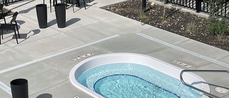 A hot tub surrounded by a patio area with chairs and tables.