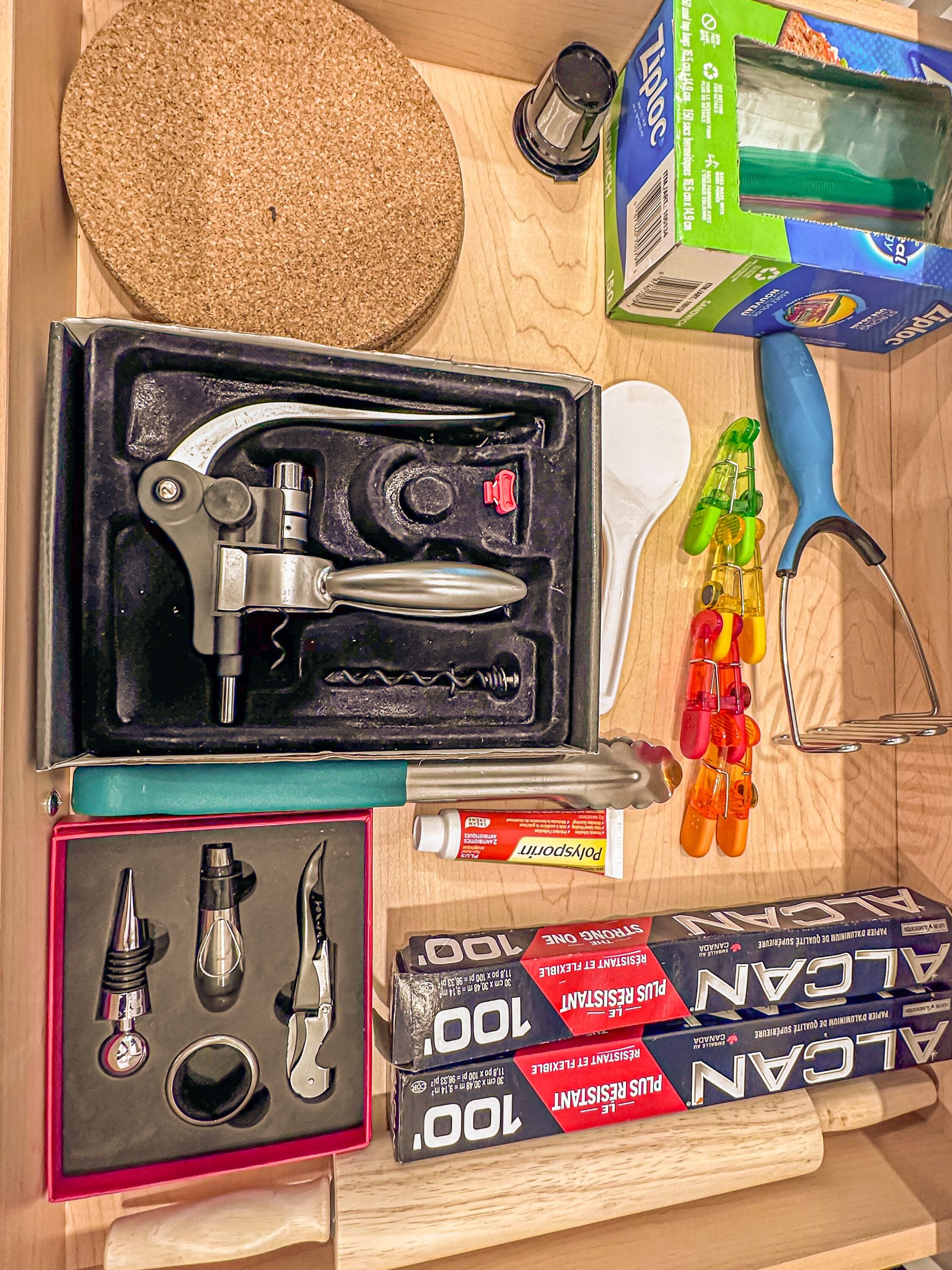 Una colección de utensilios y provisiones, incluyendo un destapador de botellas, un abrelatas y un tubo de pegamento, sobre una superficie de madera.