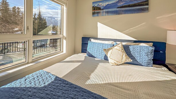 Un dormitorio con un ventanal grande, una cama con ropa de cama azul y un cuadro de un paisaje montañoso.
