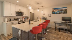 Una cocina moderna con armarios blancos, electrodomésticos de acero inoxidable, una isla grande con taburetes altos y un cuadro de un paisaje montañoso en la pared.