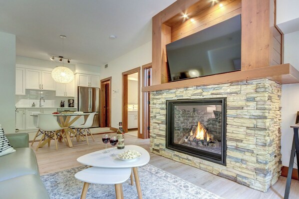 Una sala de estar moderna con chimenea de piedra, un comedor con armarios blancos y una cocina con electrodomésticos de acero inoxidable.