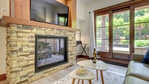 A living room with a stone fireplace, a large window with a view of greenery, and a cozy seating area.