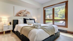 A bedroom with a large window, a bed with white linens, a dark headboard, and a wall-mounted artwork of a fox.