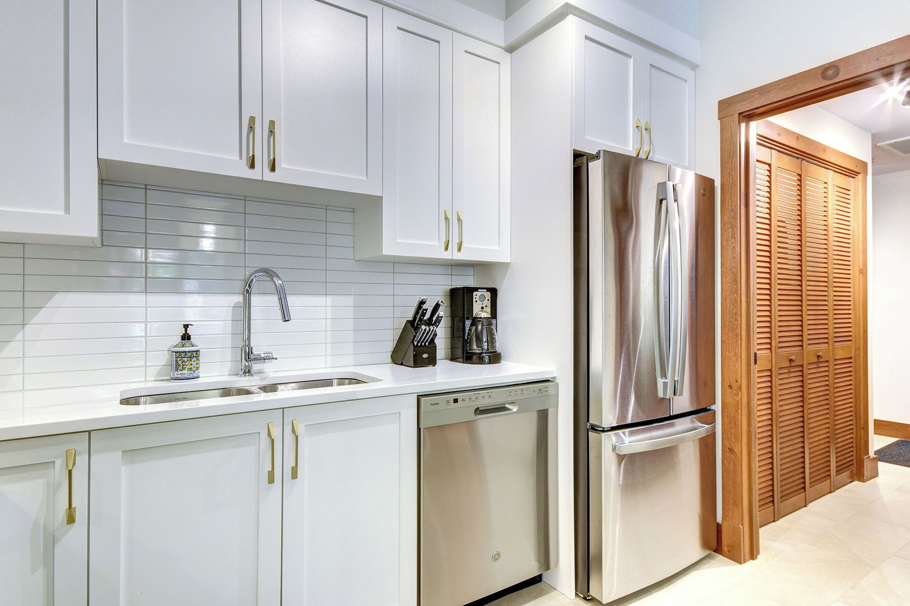 Una cocina moderna con armarios blancos, un refrigerador de acero inoxidable, un lavavajillas y una cafetera.
