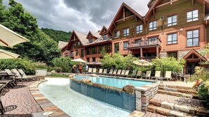 A resort with a swimming pool, lounge chairs, and a mountainous backdrop.