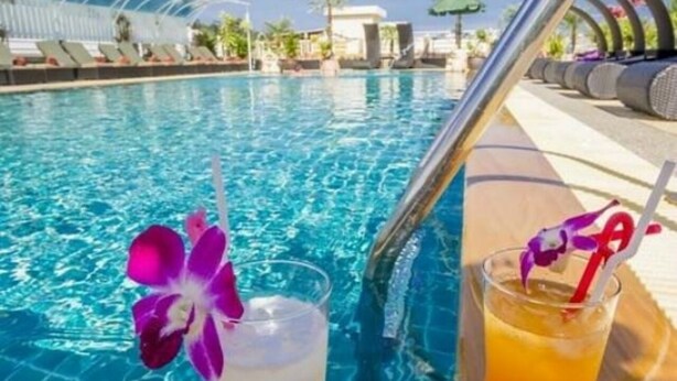 A poolside setting with two drinks, one white and one orange, each garnished with a purple flower and a straw. - Sun Shine Patong (Patong)
