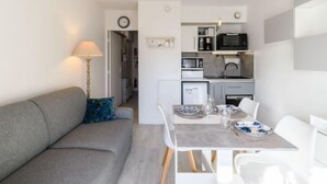 A compact living space with a kitchenette, a dining area with a table set for two, and a grey sofa with a blue pillow.