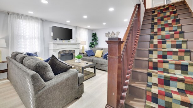 Una sala de estar moderna con un conjunto de sofá, una mesa de centro y una chimenea. Una escalera con una alfombra colorida conduce a un nivel superior.