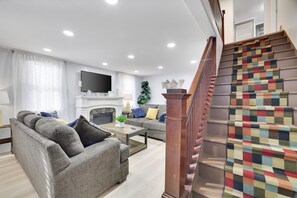 Un salon moderne avec un ensemble de canapés, une table basse et une cheminée. Un escalier recouvert d’une moquette colorée mène à l’étage supérieur.