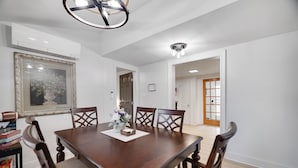 Un comedor con una mesa de madera, cuatro sillas, un florero con flores y un cuadro en la pared.