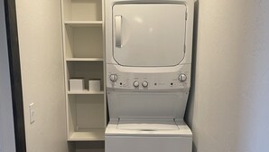 Ein Waschraum mit einer Frontlader-Waschmaschine und einem Trockner, einem Korbwäscheschrank und einem Regalsystem.