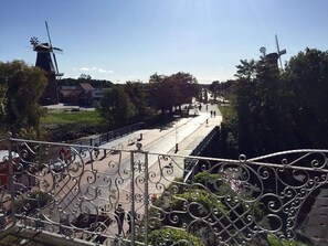A view from a balcony with a wrought iron railing overlooking a street with windmills, trees, and a clear sky.