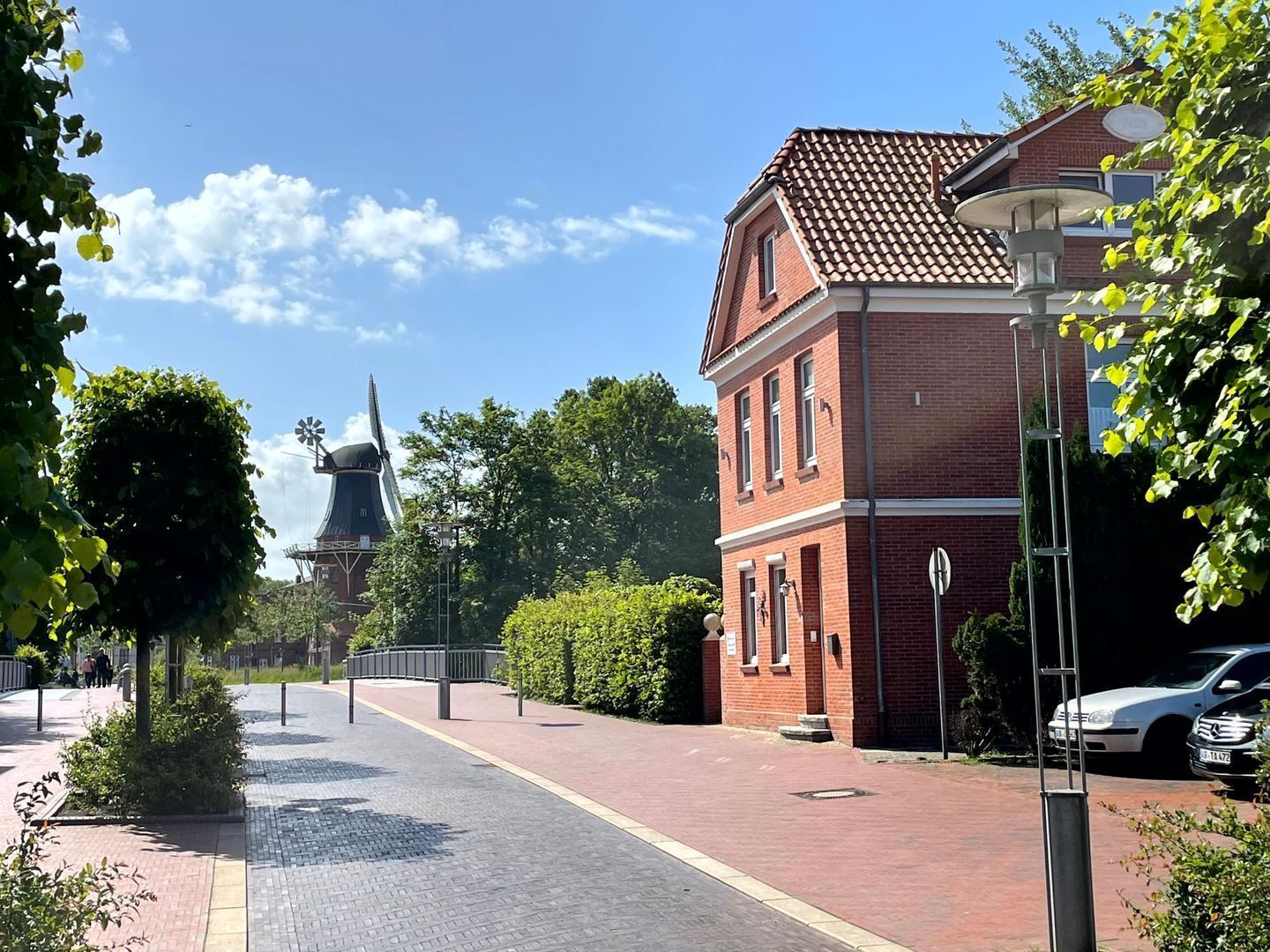 Eine Straße mit Windmühle, Backsteingebäude und parkenden Autos.
