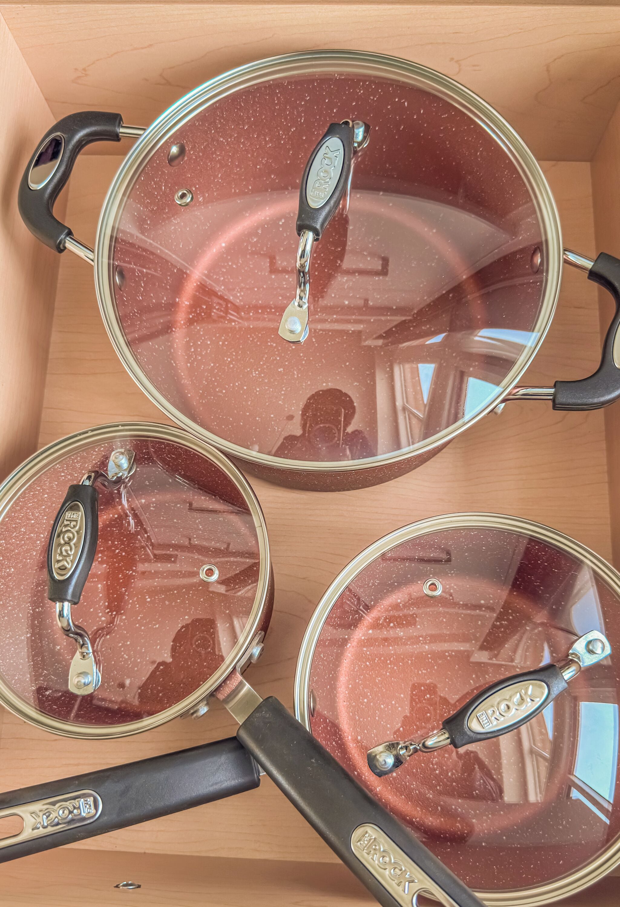 Three cookware lids with handles, placed inside a wooden box.
